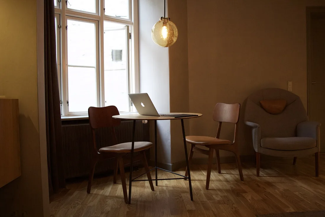 Rincón de un salón con mesa, sillas y butaca junto a la ventana, en una vivienda como las que vaciamos en Les Corts