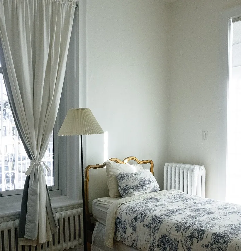 Dormitorio con cama, cortinas y radiador, en una vivienda como las que vaciamos en Sant Adrià de Besòs
